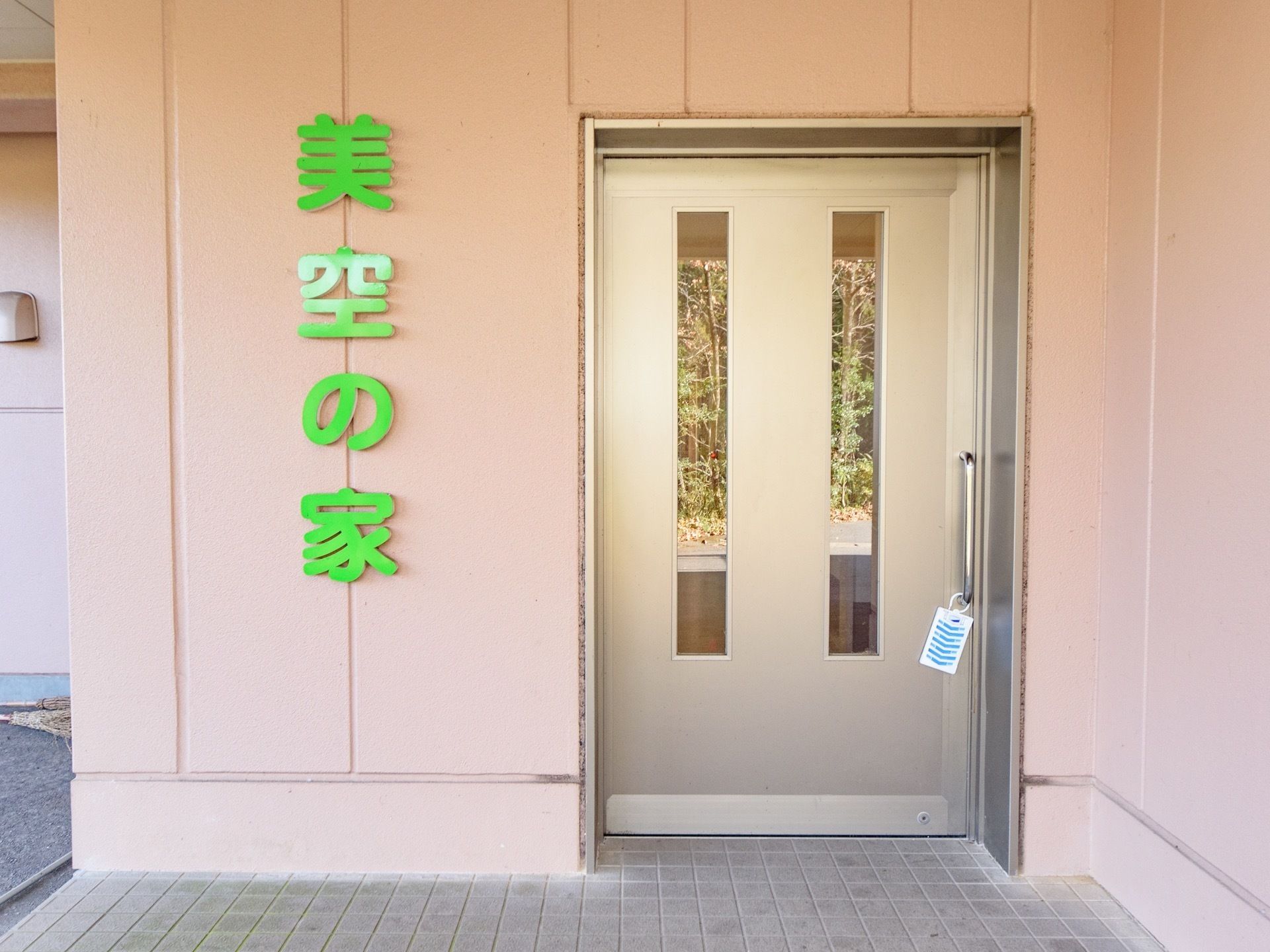 玄関ドアの横の壁には大きな黄緑の文字で施設名が記されている。スライド式の扉は間口が広い。屋根がついている。