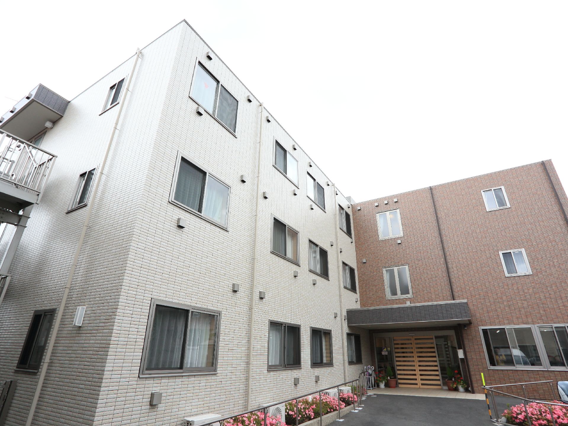 3階建ての建物。外壁は、白色と茶色からなる。エントランスは茶色の自動ドアになっている。建物の脇には、木花が植えられている。
