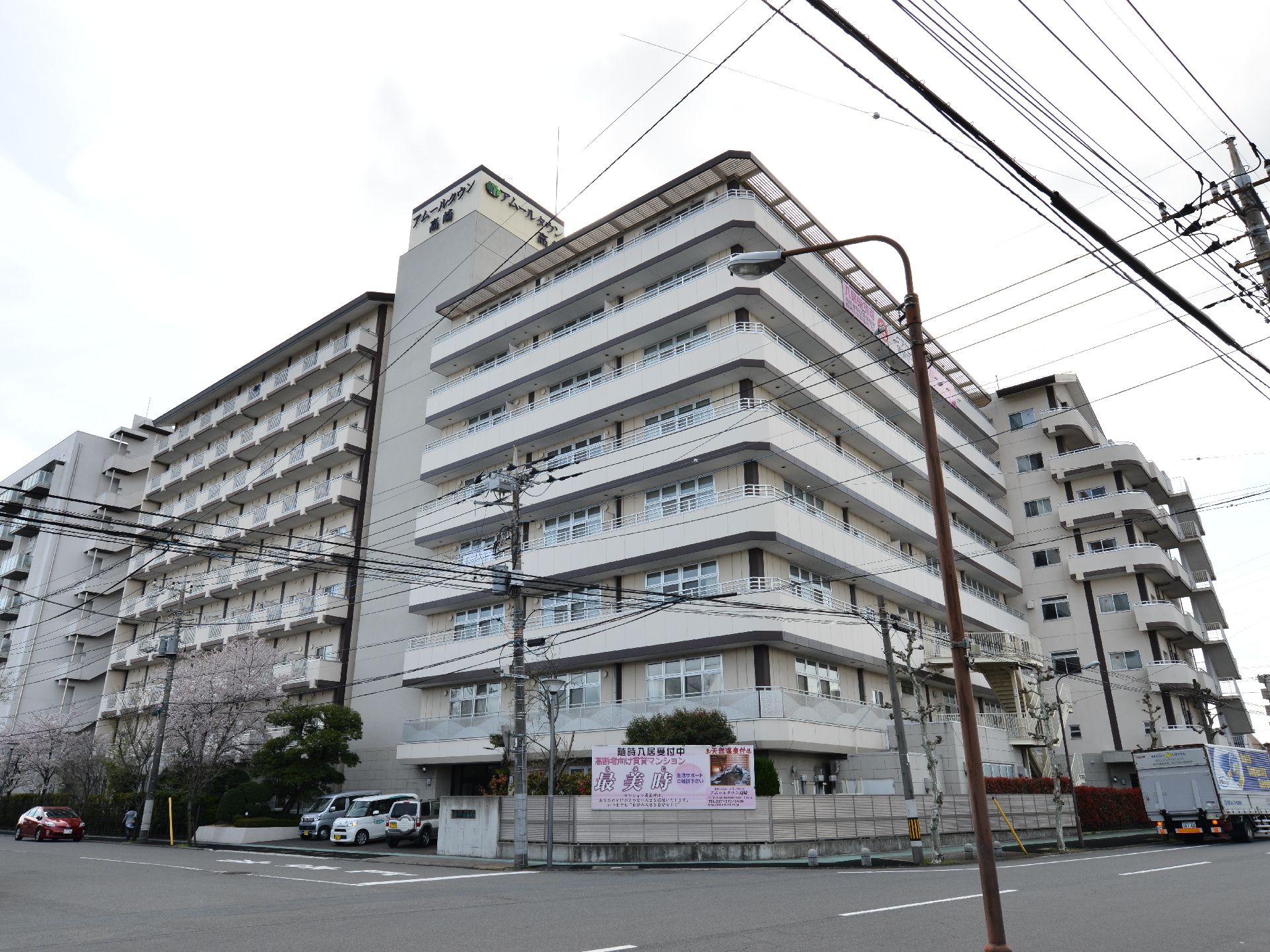 施設の目の前は広い道路となっており、正面に施設名が書かれている看板が掲げられている他、車も数台停まっている。