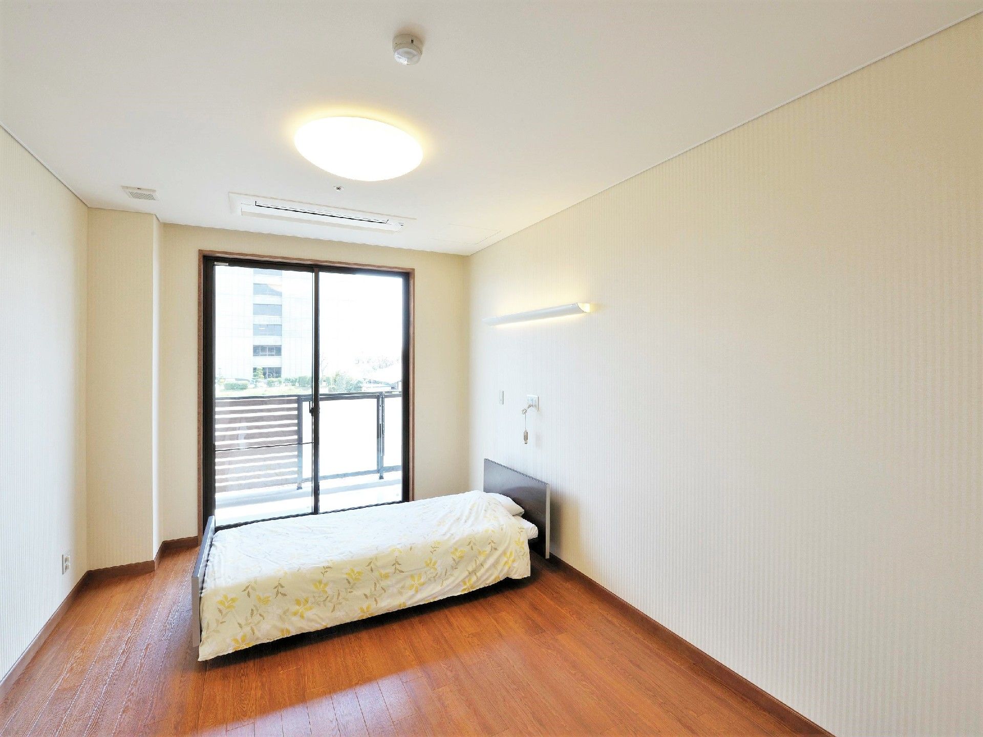 ベランダが付いた居室はフローリングで、寝具付きのベッドと緊急通報装置が設置されている。