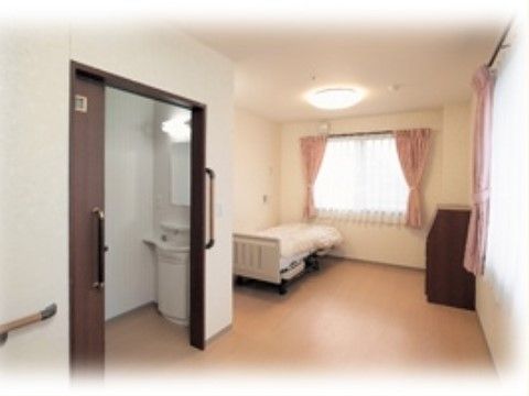 居室内の壁やトイレのドア前には手すりを付けてある。２ヶ所に窓があり、ピンク色のカーテンがかかっている。