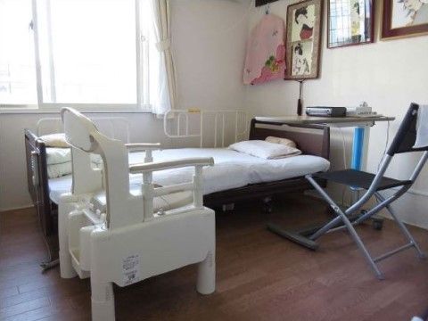 介護用のベッドが置かれた居室。ベッドの横には、サイドテーブルや椅子、ポータブル式の洋式トイレが置かれている。