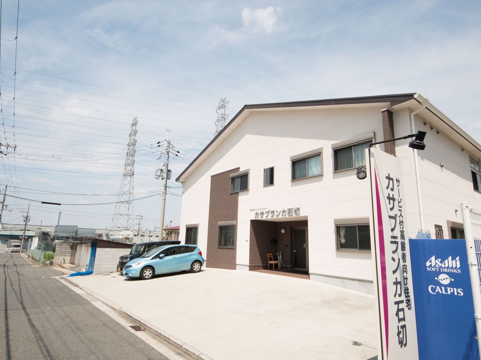 二階建ての建物で、玄関の上部分の壁にシルバーの文字で施設名が表示されている。建物の前に駐車スペースが整備されている。