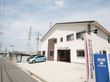 二階建ての建物で、玄関の上部分の壁にシルバーの文字で施設名が表示されている。建物の前に駐車スペースが整備されている。