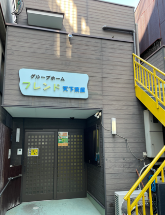 建物の前方には黄色い手すりが印象的な外階段が設置されていて、２階へと上がることができる。入り口にポストが設置されている。
