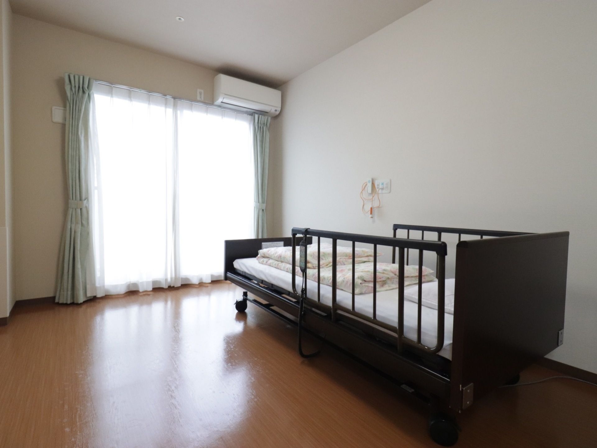 大きな窓から光が差し込む、ゆとりのある居室である。移動式の介護用ベッドが設置されており、清潔感のある明るい部屋となっている。