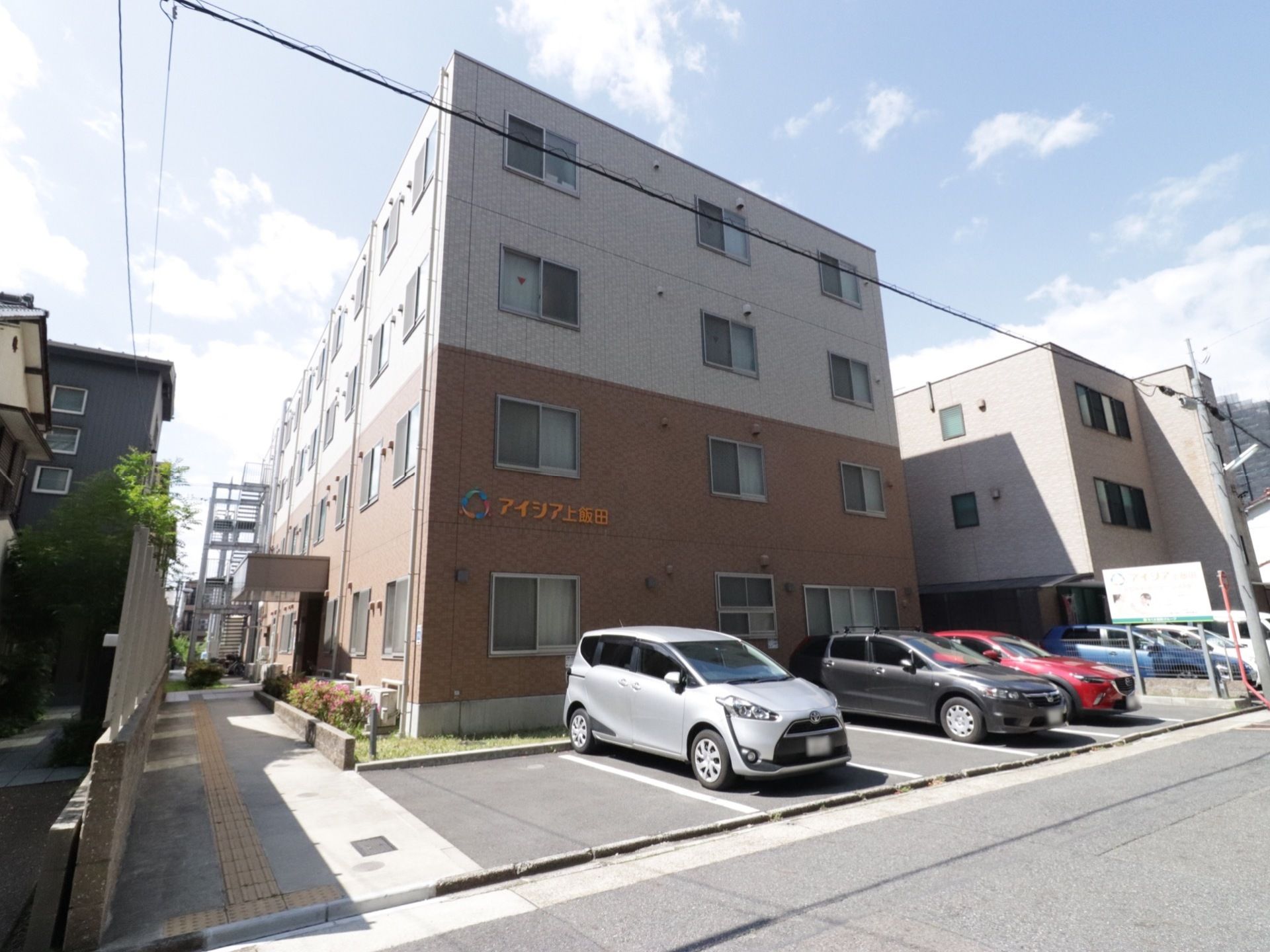 施設の建物は４階建てのボックス型ビルのような外観で、２階と３階の境目で外壁の色を変えている。建物の前には、敷地内に駐車場がある。