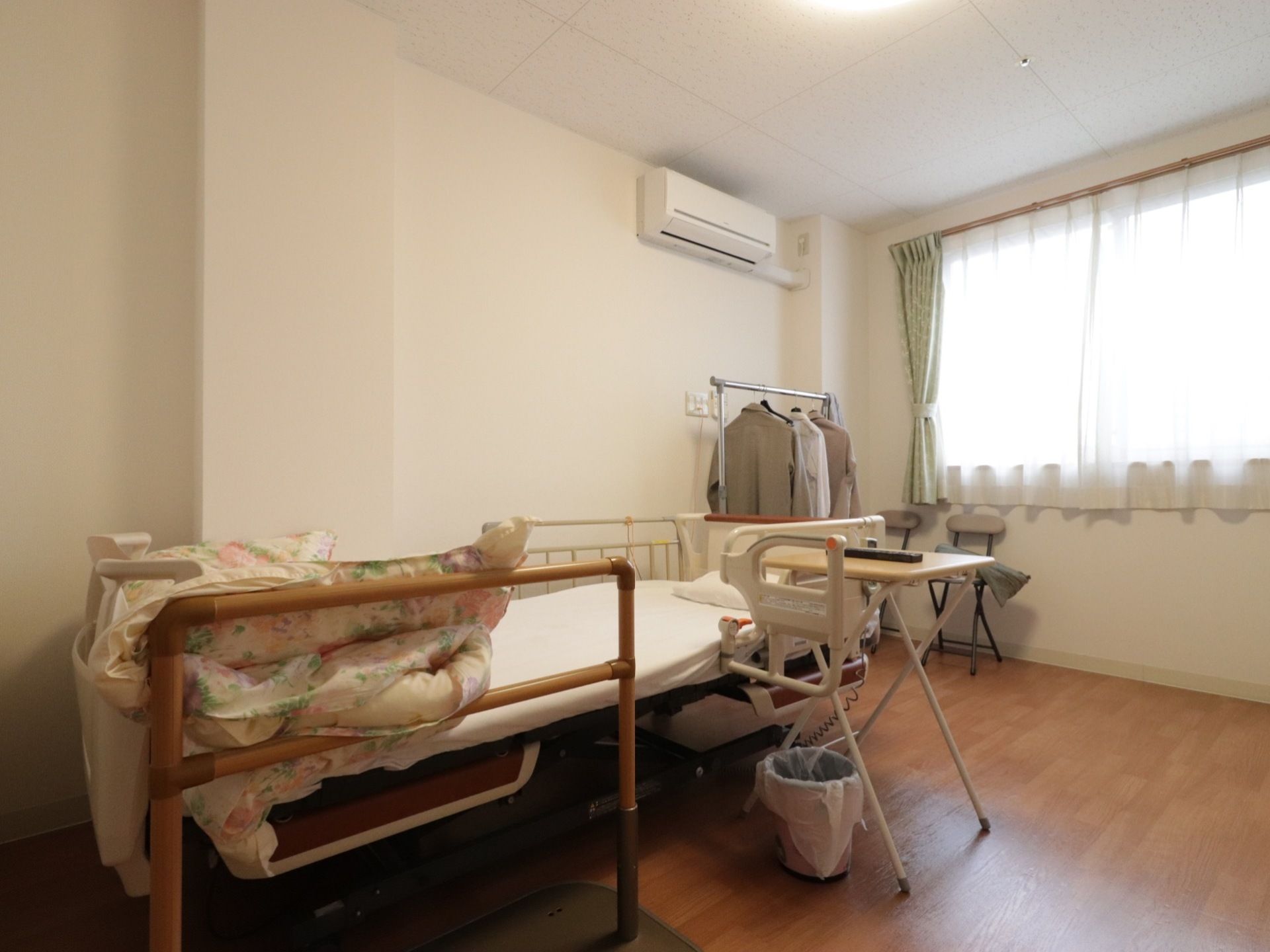 あたたかみのある照明が明るい居室。壁際に介護用ベッドが置かれている。落下防止のため、ベッドは安全柵が取り付けてある。