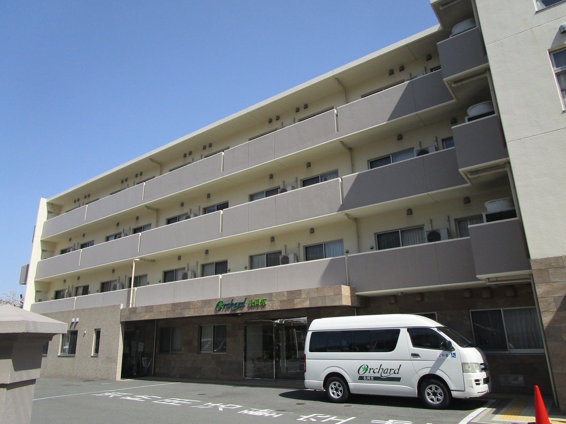 4階建の白い建物で周辺は広く、メイン道路に面していて車での乗り入れがスムーズ。 施設はメイン道路に面しているので、車での来所が便利である。