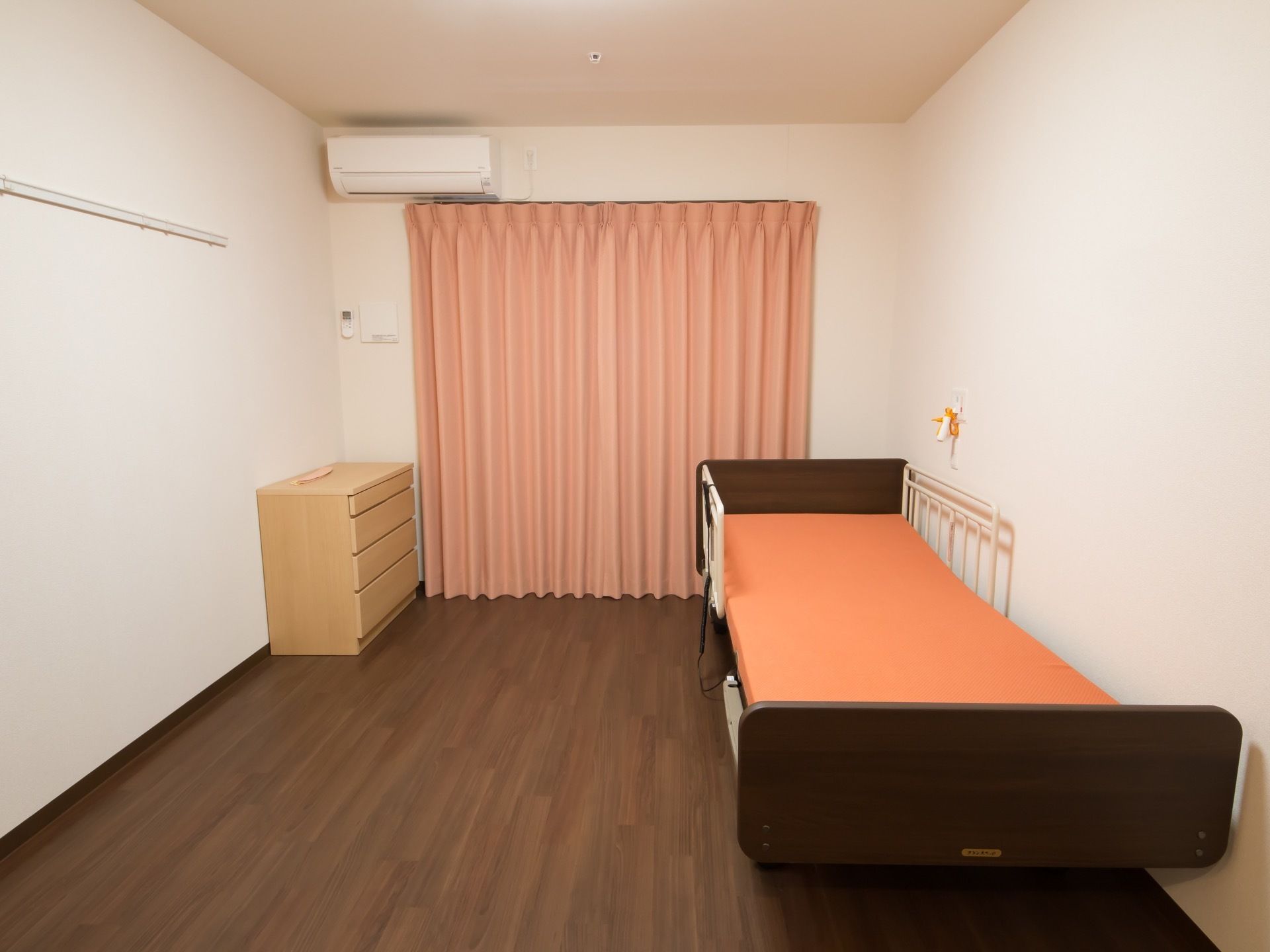 居室のカーテンは暖色系の厚手のものが使われている。左側の壁には白く長いハンガーバーが取りつけられている。