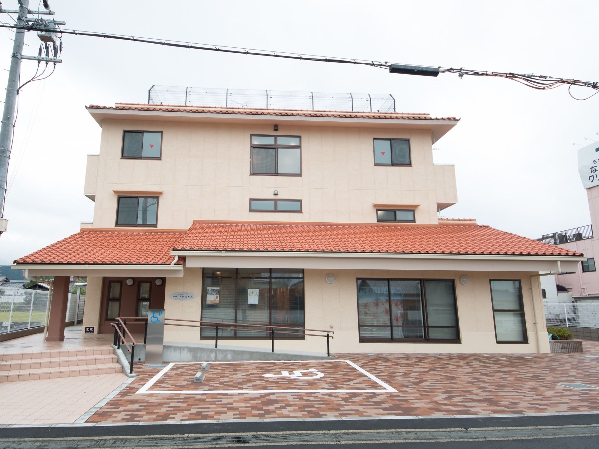 施設建物を正面から見たところである。手前にあるブロック舗装の敷地内には、車椅子専用の駐車スペースが用意されている。