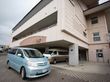 １階部分に駐車スペースがあり、車が停まっている。建物はベージュの外装で、敷地はレンガが敷き詰められている。