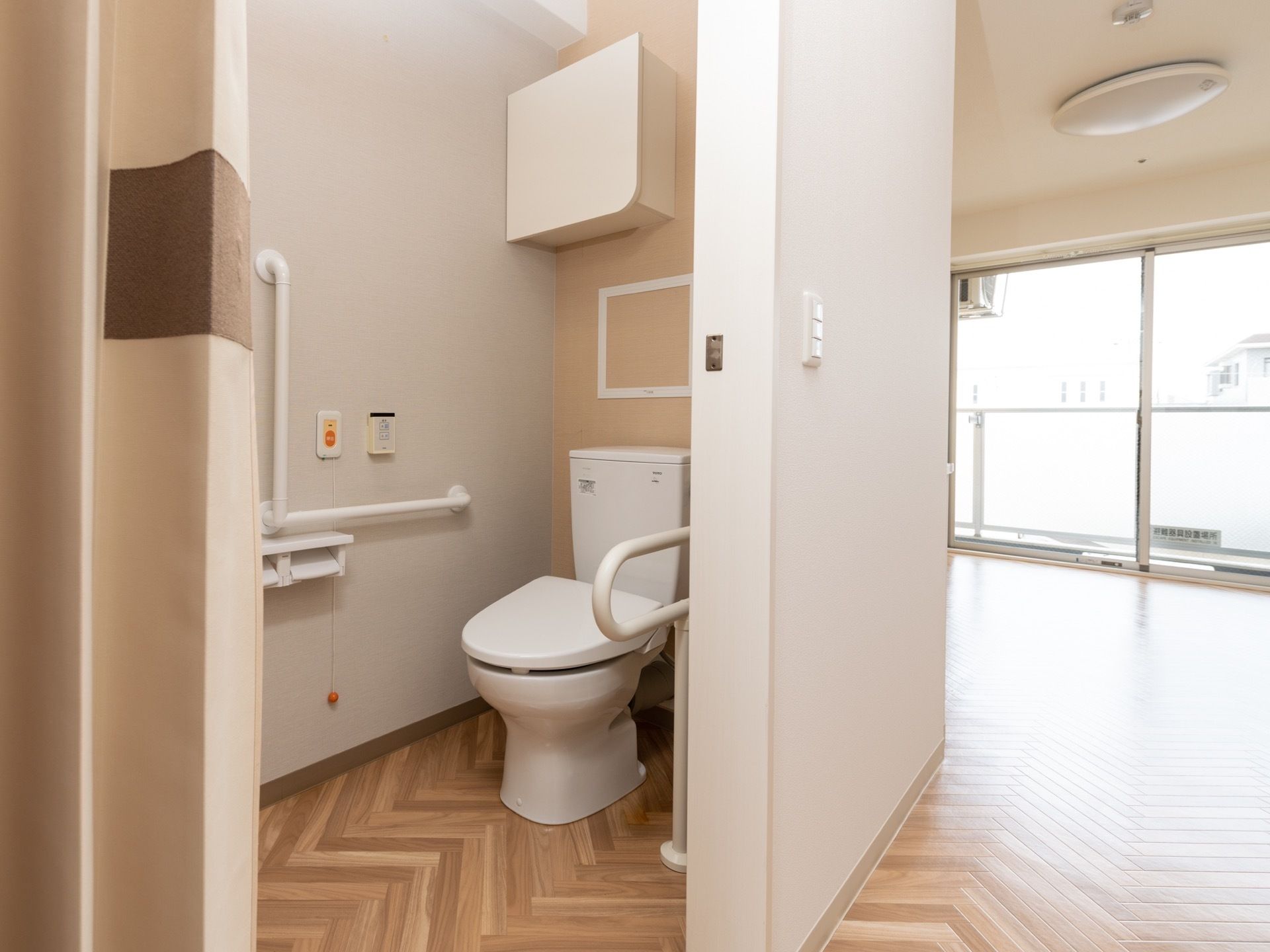 トイレは広く手すりが付けられている。緊急用のボタンもある。部屋の奥には大きな窓がある。ベランダもある。