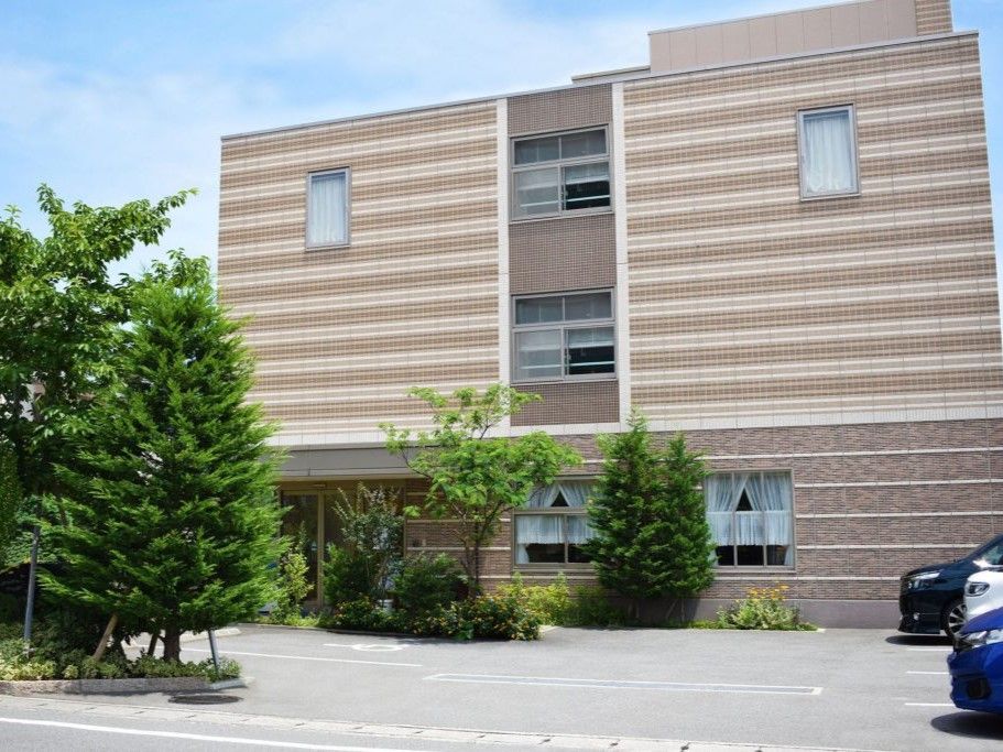 施設は、ベージュとブラウンのボーダー柄の外壁が特徴的な３階建ての建物である。駐車場が建物前に設けられている。