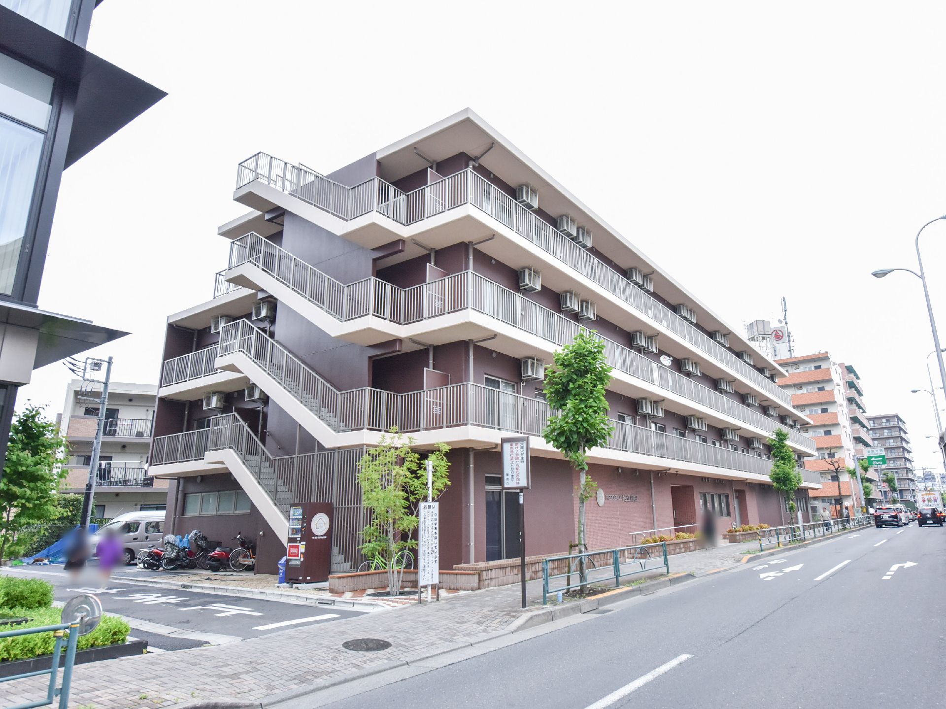 施設建物の外観。パイプ型の手すりのある非常階段のような通路が暗褐色の外壁に沿って張り巡らされているのがわかる。
