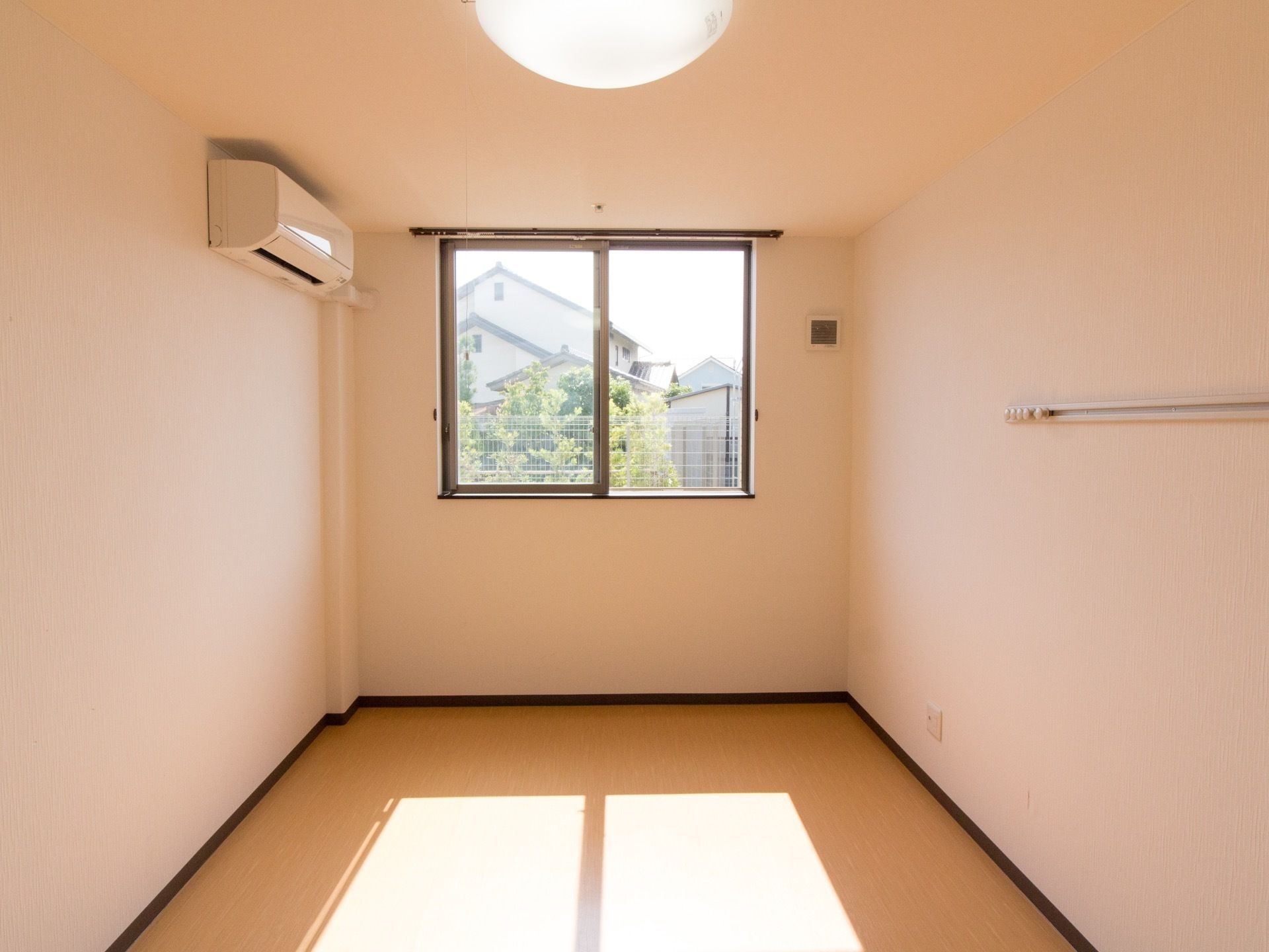 何も置かれていない日当たりの良い、お一人様用の居室である。窓とエアコン、電灯、ピクチャーレールが備え付けてある。