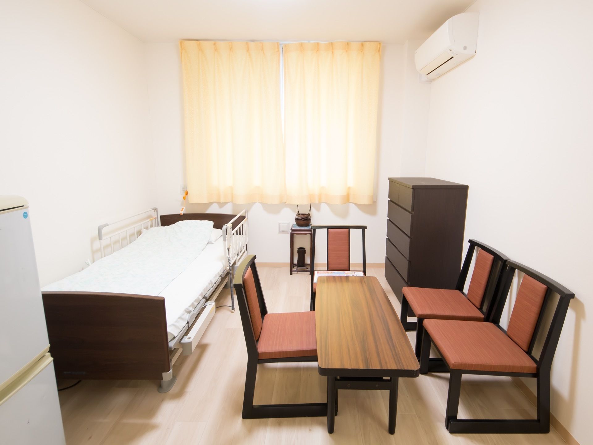 明るい色合いのフローリング部屋である。ベッドやチェストが置かれているほか、テーブルや椅子も設置されている。
