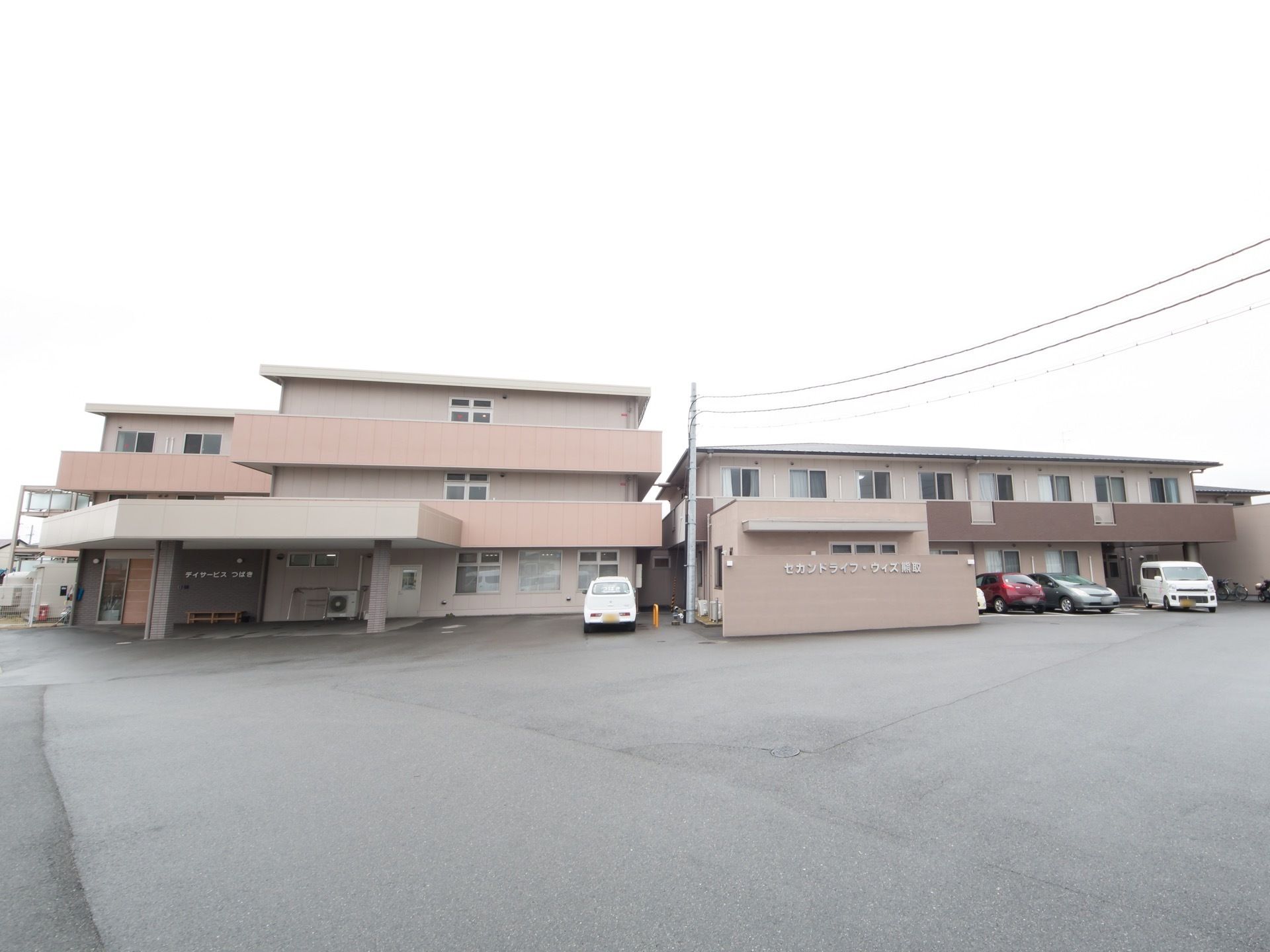 広々としたアスファルト敷地である。駐車場も完備されている。３階建て、２階建ての施設が隣同士に建っている。