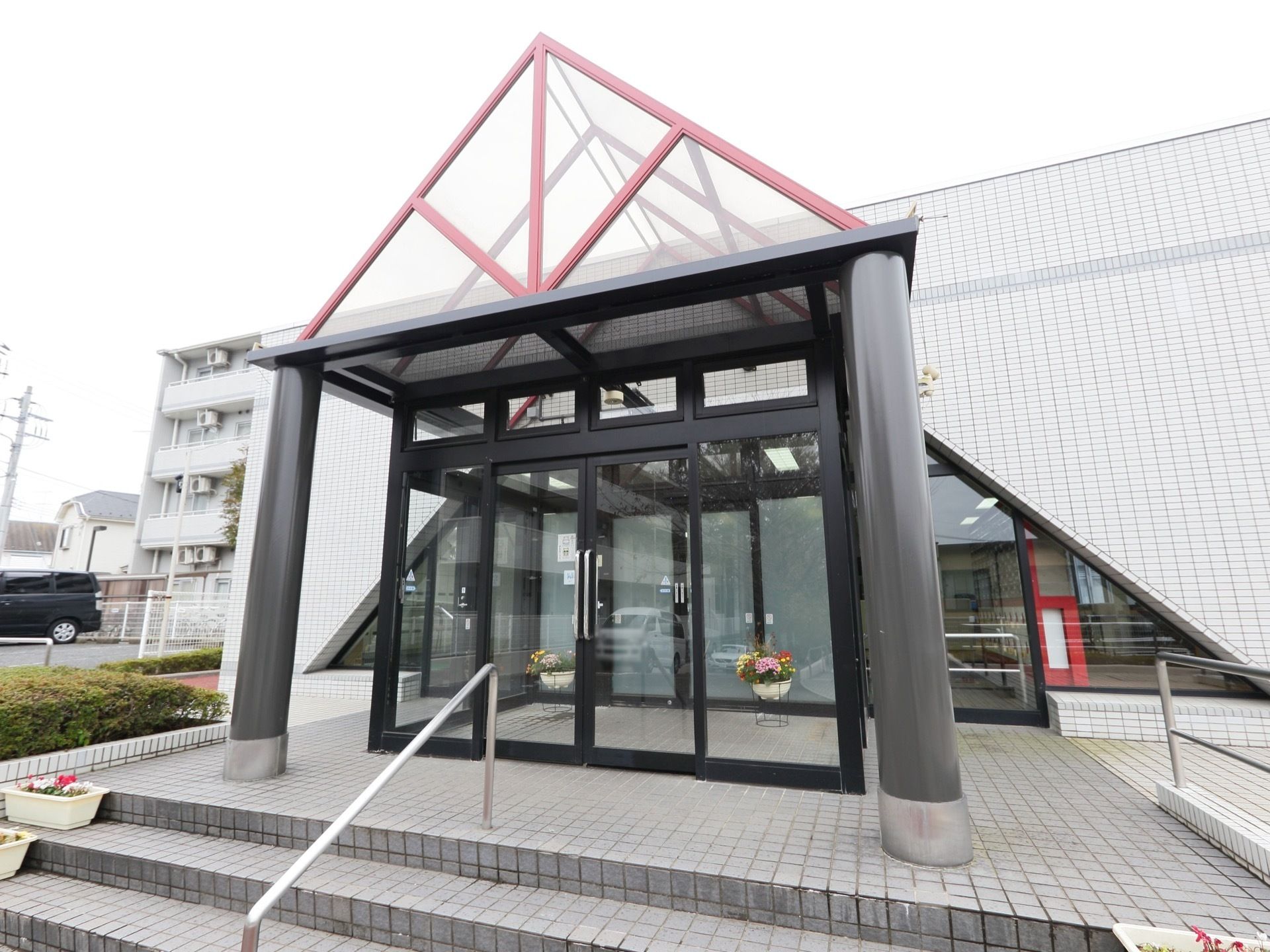 玄関ドアの上には三角形の赤い屋根があり、モダンな雰囲気になっている。白いプランターに、さまざまな花が植えてある。
