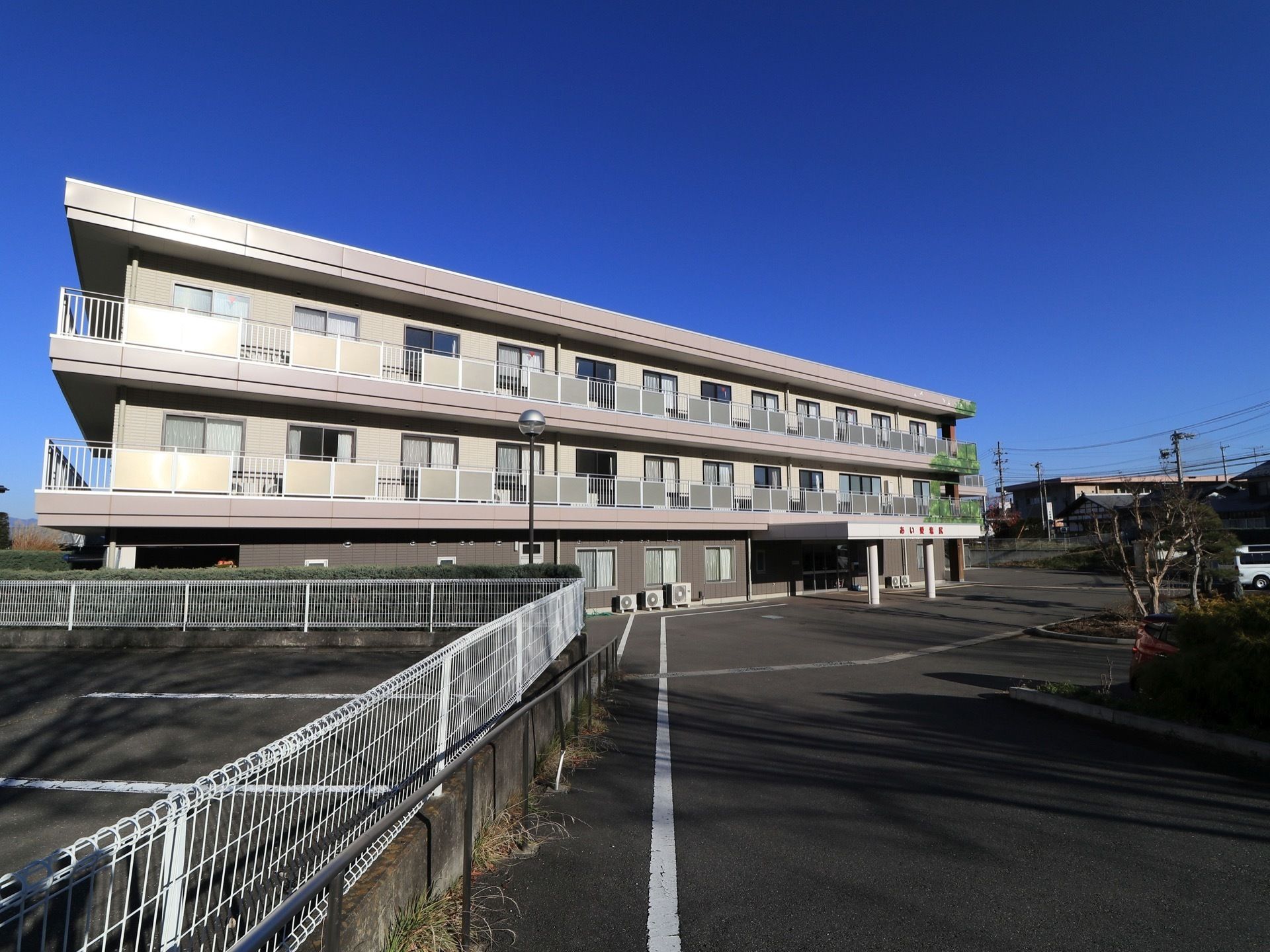 施設は居住部分にバルコニーが備わった３階建ての建物である。建物前には、広い駐車スペースが設けられている。