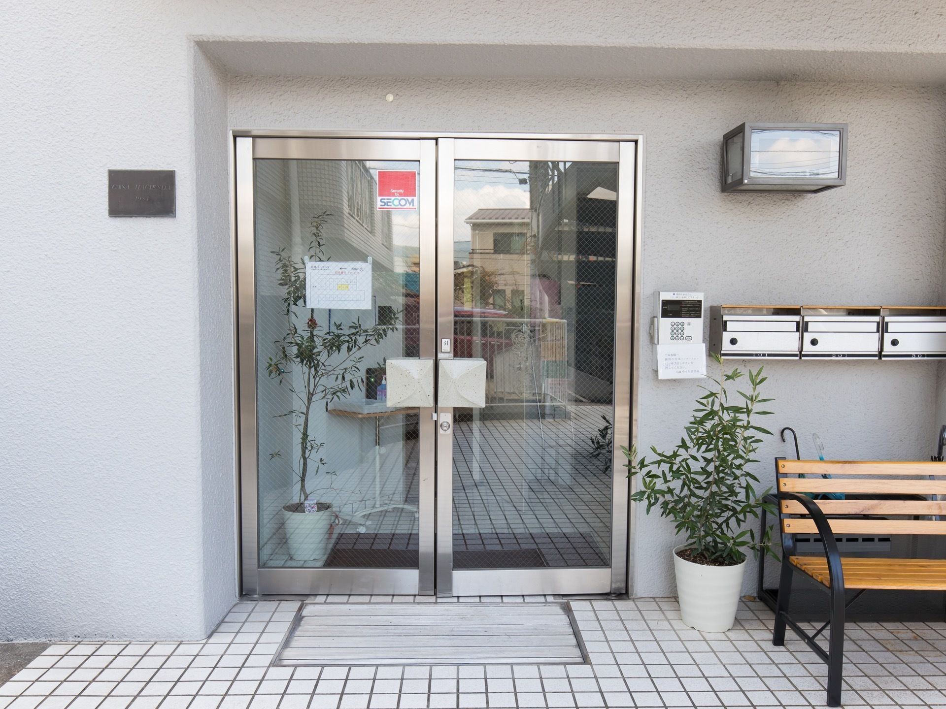 玄関は2枚の開き戸タイプを採用している。床はグレーのタイル張り。観葉植物のとなりにはベンチが置かれてある。