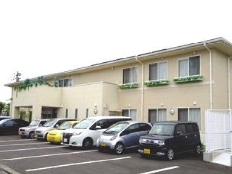 ２階建てのホームには、バルコニーがあり、窓辺は緑に彩られている。建物前には駐車スペースが設けられている。
