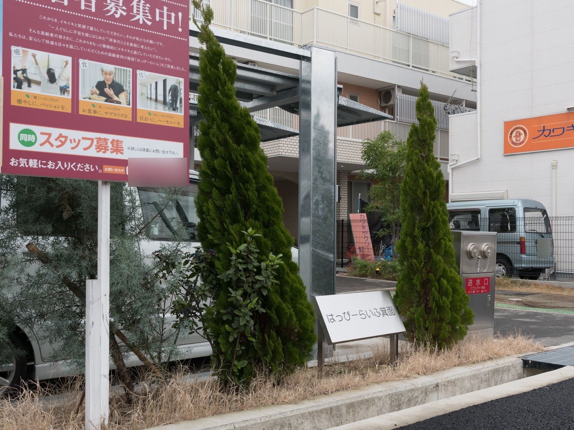 入居者やスタッフを募集した看板が立てられている。たくさん植物が植えられている。消火栓が設置されている。