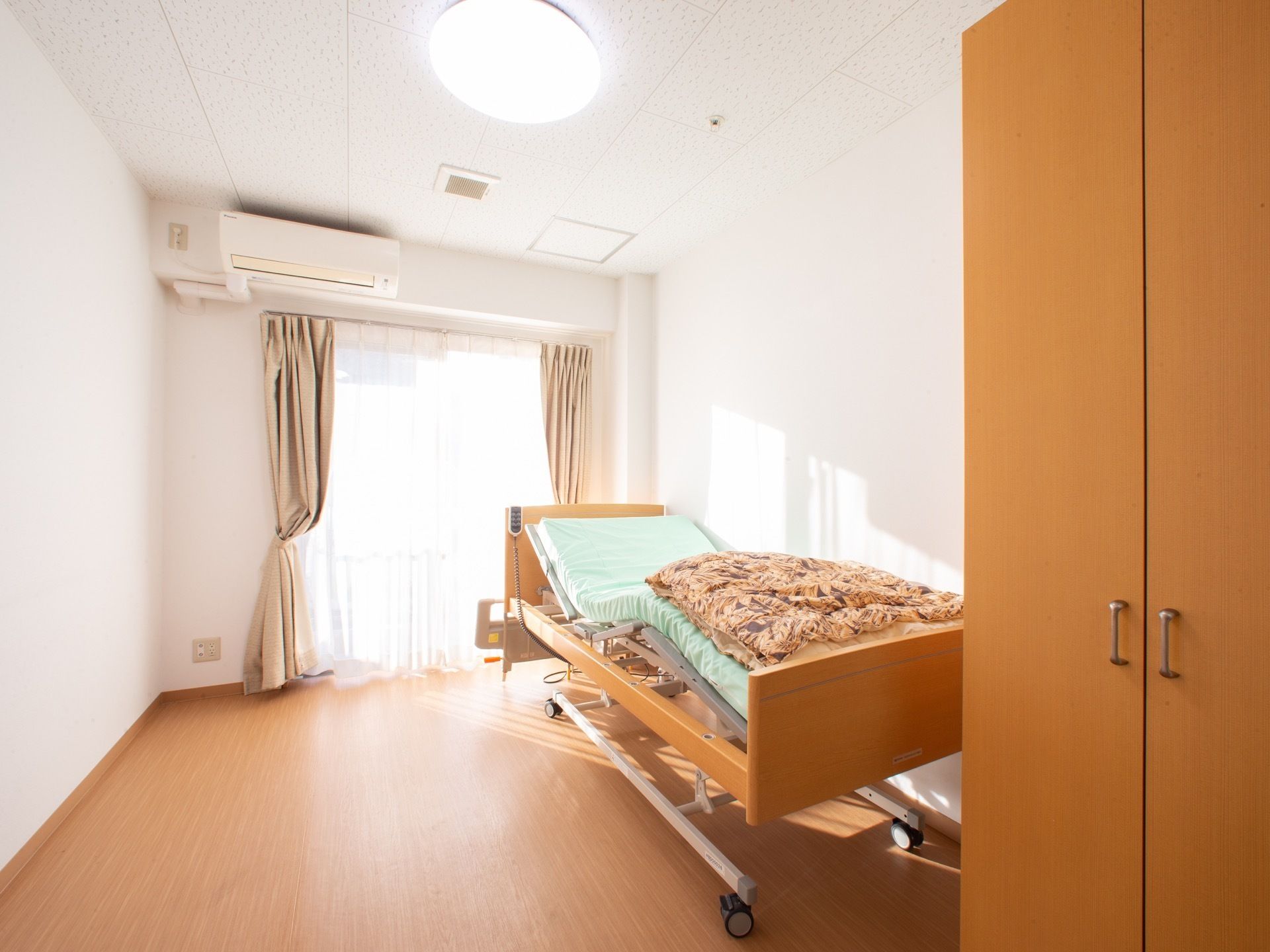 窓からは日の光が差し込み明るい。介護用ベッドが置かれている。エアコンも完備されており、快適に過ごせる。