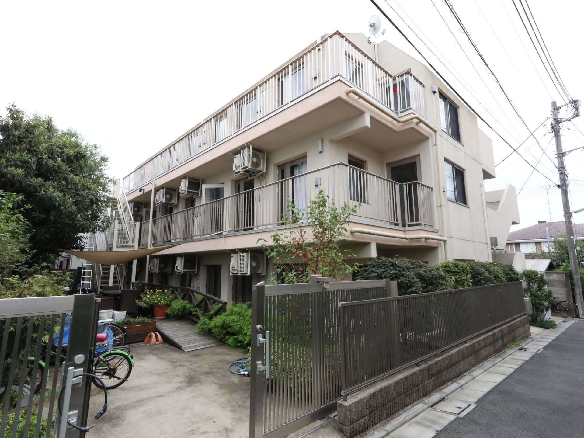 ３階建てであり、鉄製の門を抜けるとすぐ敷地内には自転車が停まっている。奥の通路は植物が育ち、緑豊かである。