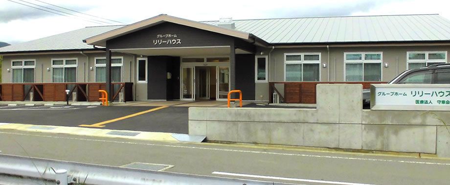 平屋建ての建物で玄関には屋根が付き、外壁にはホーム名が書かれている。駐車場も広い。
