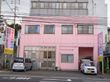 施設の外観はピンク色で、窓には青とピンクの花の飾りが貼られている。施設の前に数台の駐車スペースがある。