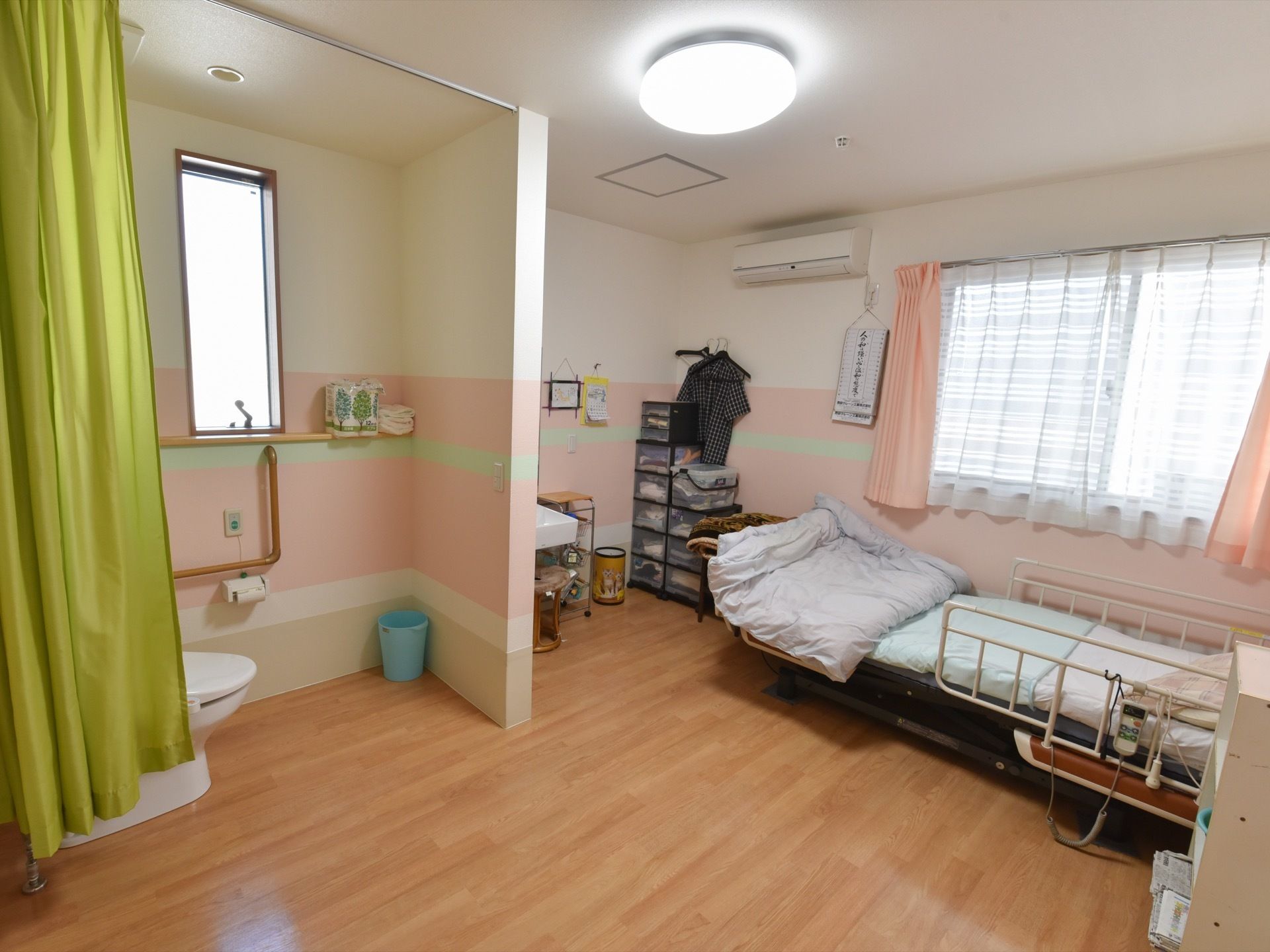 ピンクの壁とピンクのカーテンが明るい雰囲気の広々とした居室にはトイレや洗面スペースが設けてあり、トイレは扉のないカーテン式になっている。