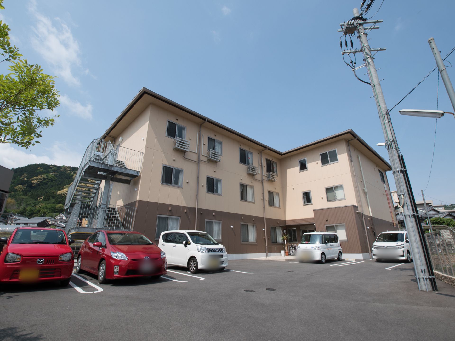グループホームの入り口にはクルマが停められるスペースがある。また奥にも20台ほどの駐車場が設置されている。