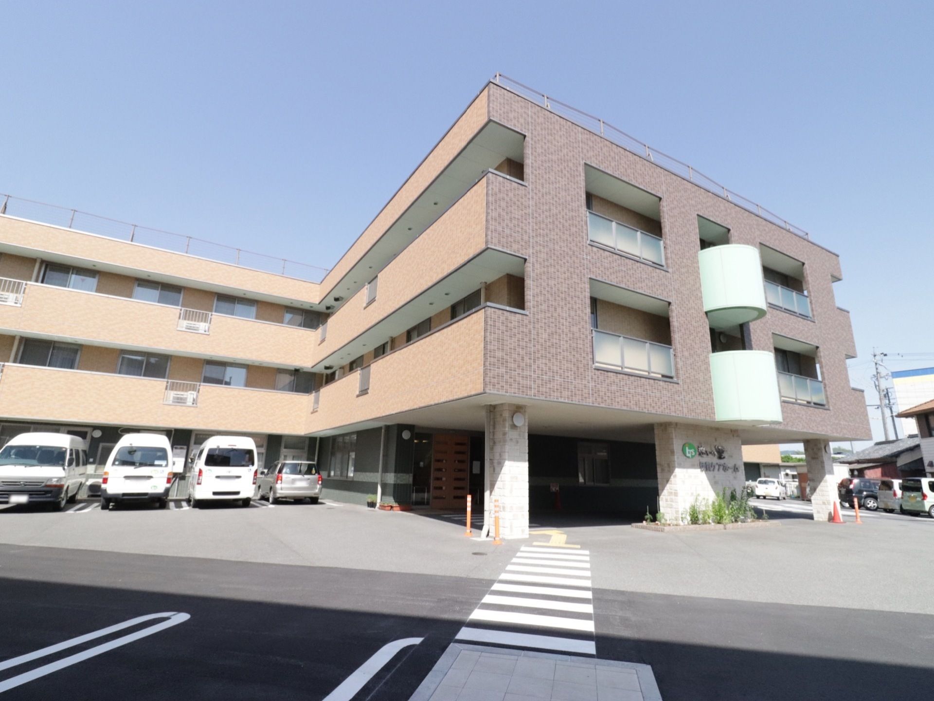駐車場は広く、施設の外壁はタイル貼りで、茶色と黄土色のタイルが貼られている。施設の玄関前には施設名が書かれた看板がある。