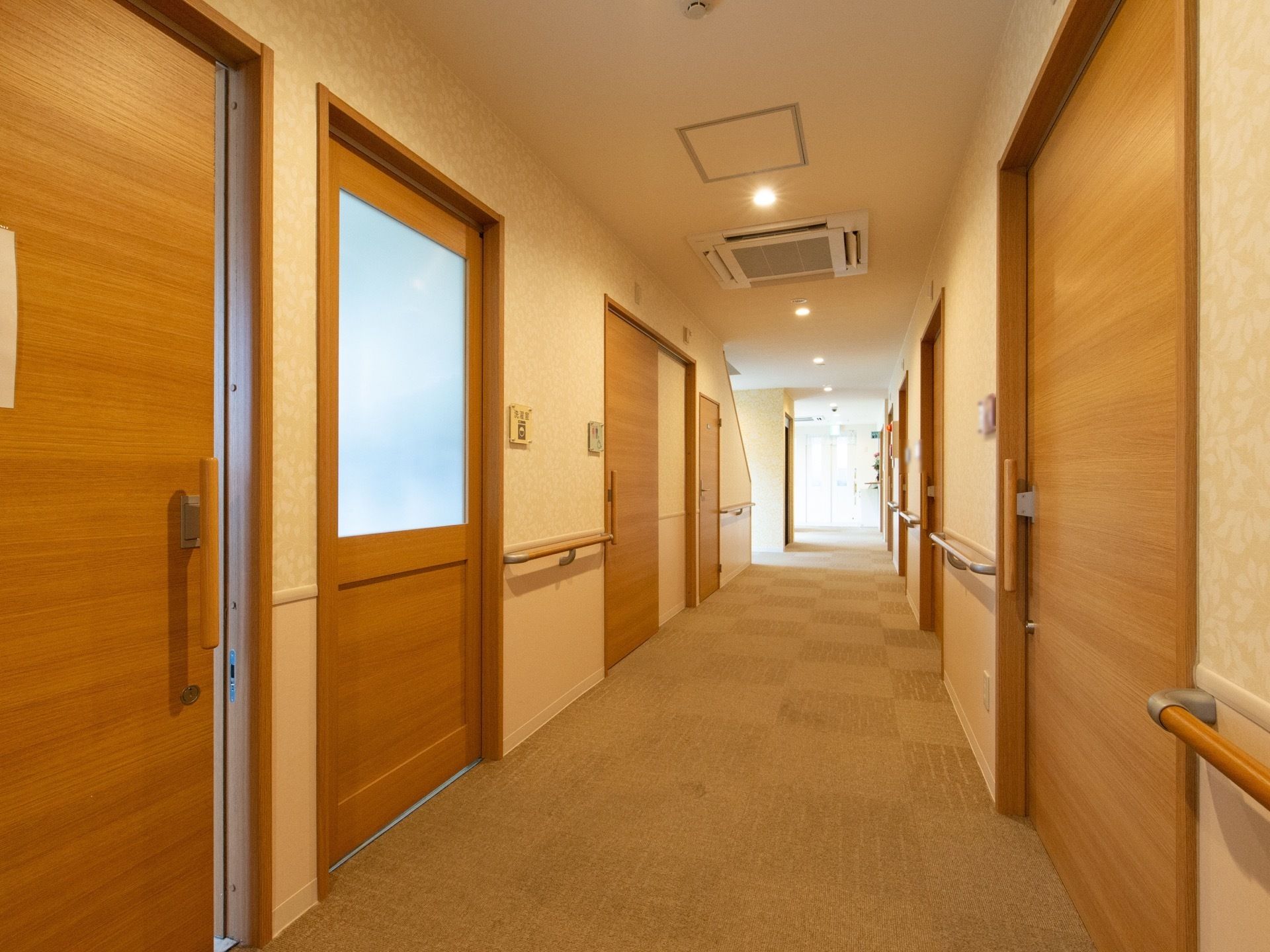 通路の両側には木目調のドアが並んでおり、手すりが設置されている。天井には火災報知器や空調が取り付けられている。