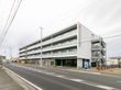 ４階建てのマンションタイプの建物である。向かって右側に、玄関や駐車場入り口がある。角に自動販売機が置かれている。