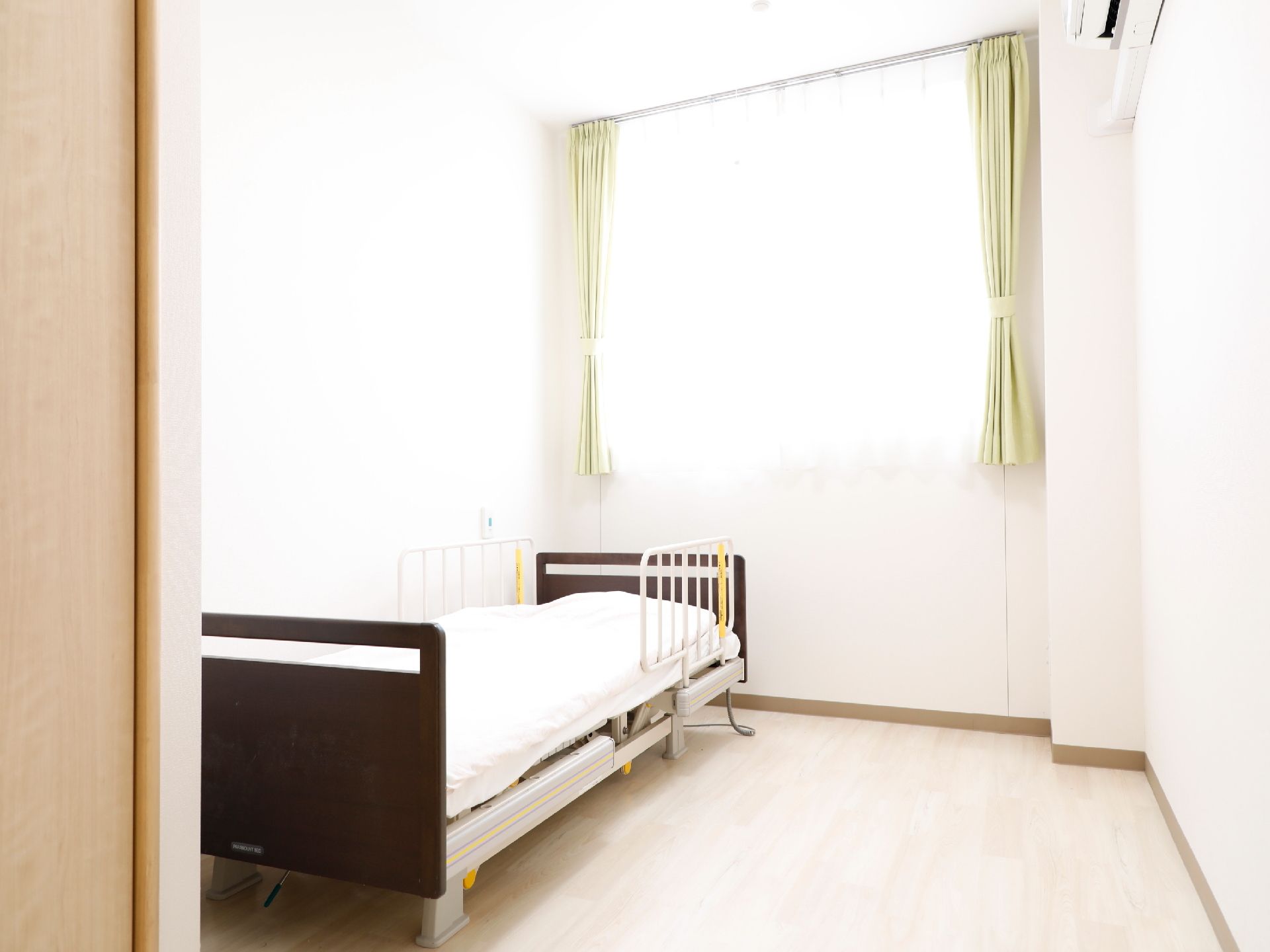 ワンルームの洋室で、壁には緊急時にスタッフを呼ぶことができるブザーが設置してある。電動式のベッドが一台置いてある。