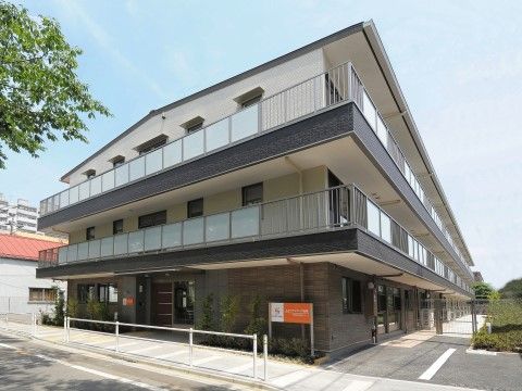 3階建ての施設が建っており、その手前には道路が通っている。玄関の上には屋根があり、雨天時などでも気にせず出入りできる。