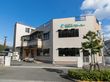 落ち着いた色合いの２階建てのグループホーム。玄関前にはスロープが設置されており、その横にはベンチが置かれている。