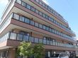 施設は５階建てのモダンな建物である。建物の前が駐車場となっており、数台が停まっている。駐車場の横に庭木が植えられている。