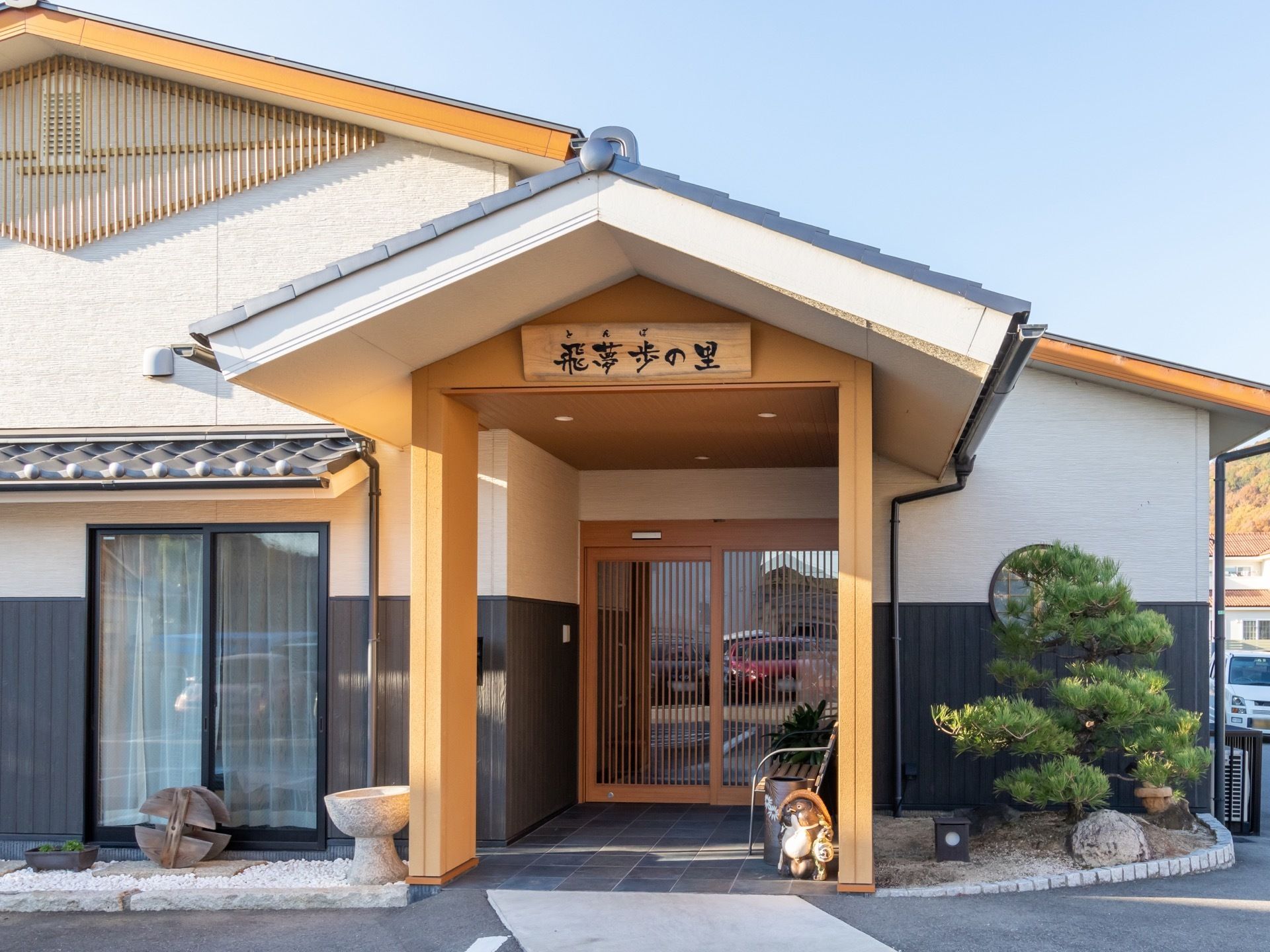 玄関までの通路には屋根が取り付けられており、強い夏の日差しなどを防ぐことができる。玄関の脇には木々が植えられている。
