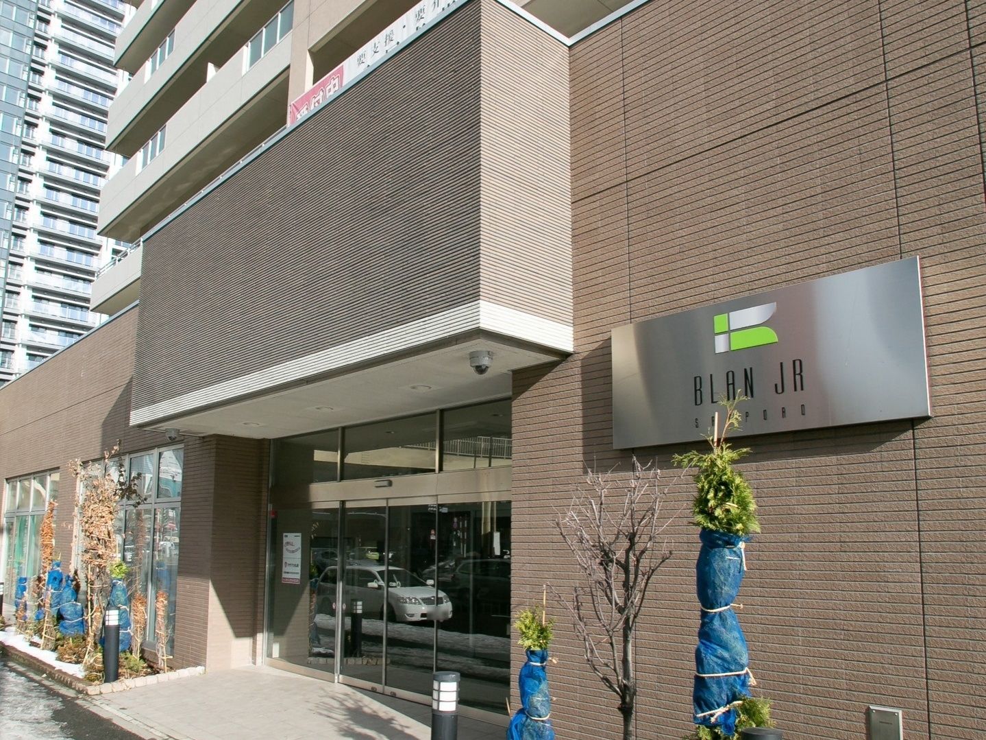 太陽の日差しが、建物全体に届いている。外壁は落ち着いたブラウン。玄関の扉は、自動ドアが備えつけられている。