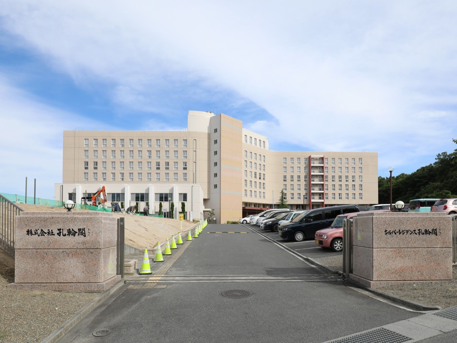 駐車場、施設へとつながる道路の門が開かれた状態になっている。右側に駐車場が広がっており、左側では工事がおこなわれている。