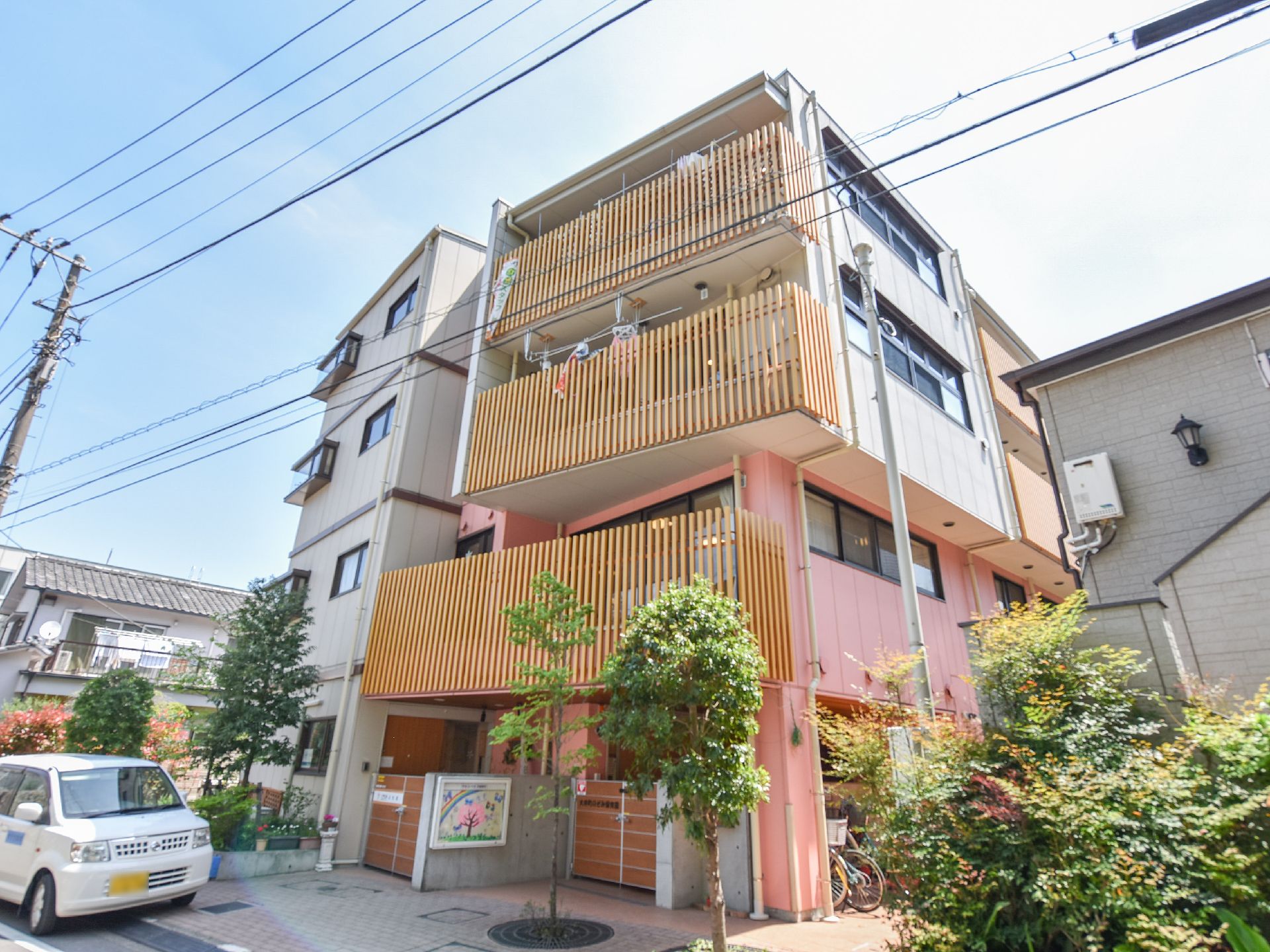 薄いピンク色や、クリーム色などの優しくあたたかい色合いを基調とした建物となっている。ベランダは木の格子の手すりになっている。