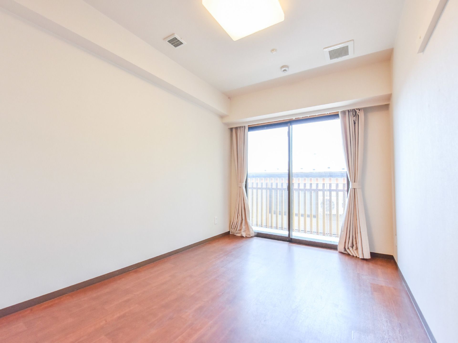 部屋にはベランダに出ることができる大きな窓があるため、室内は明るく過ごしやすい。クリーム色のカーテンが保温効果をアップ。