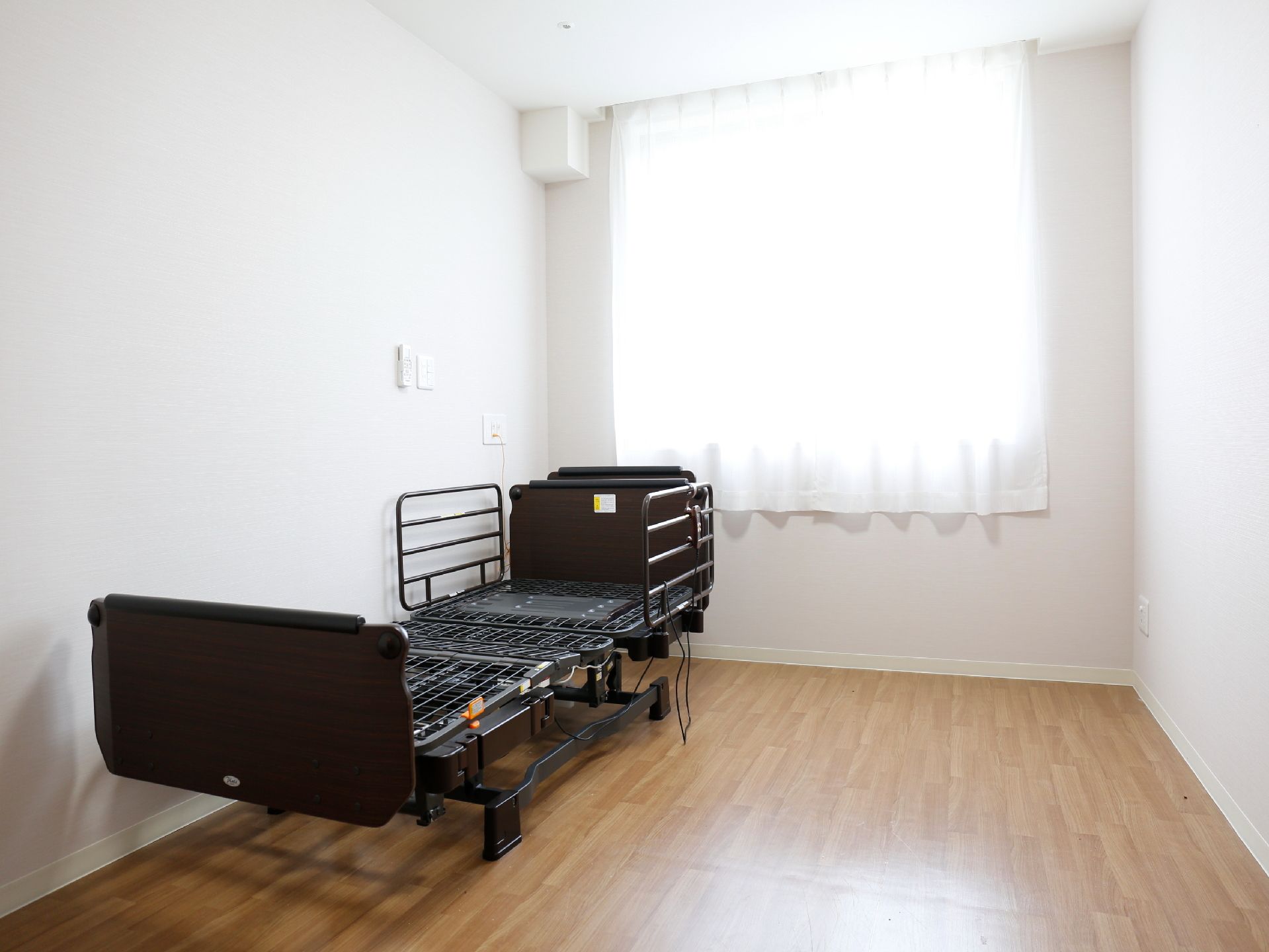 白壁とフローリングのシンプルな部屋に介護ベッドを設置しています。入居者が家具や雑貨を自由にレイアウトし居心地の良い空間を作ることができる。