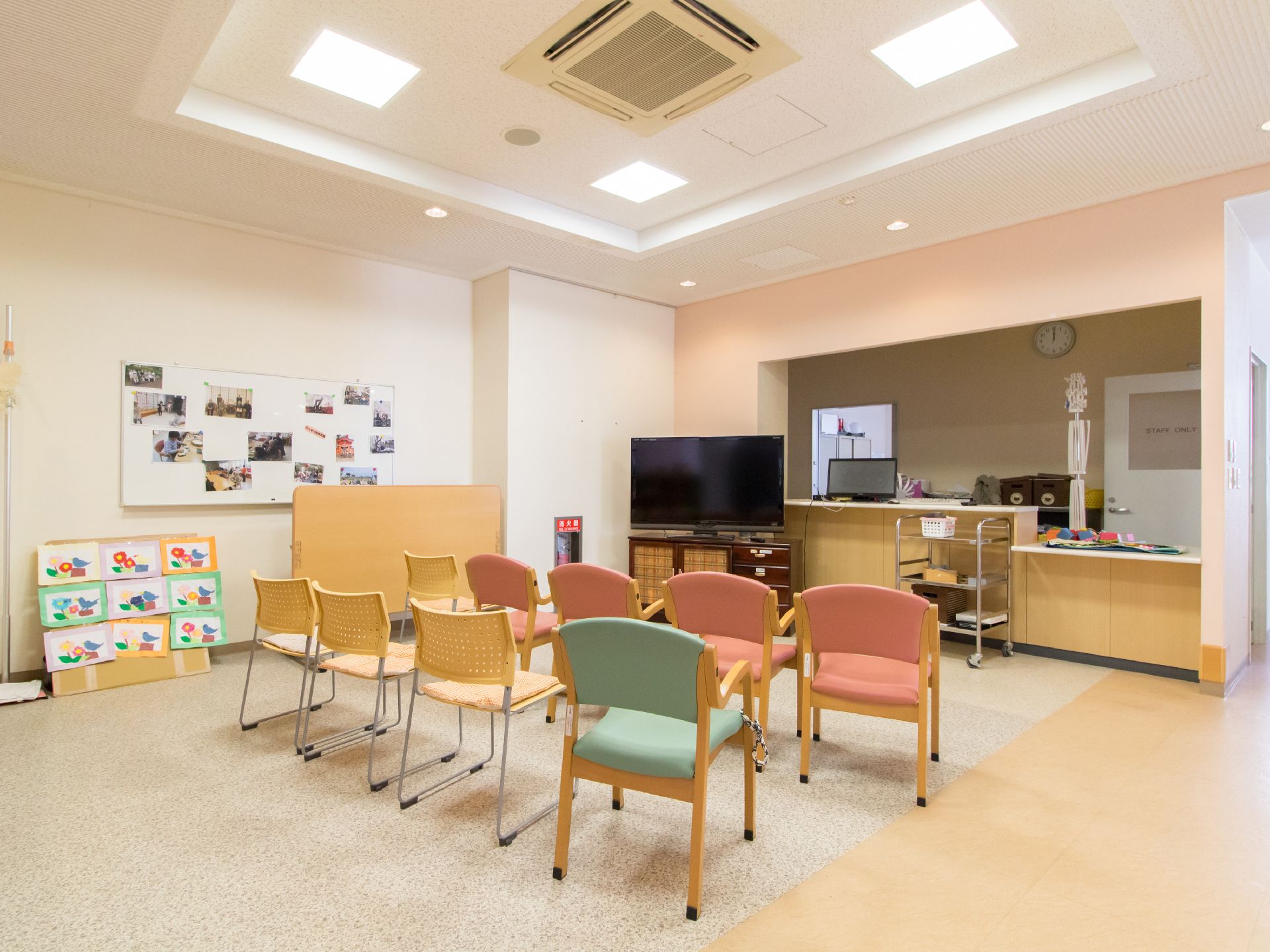 フラットなフロアに複数の椅子が並べられている。部屋のコーナー部分にはテレビがあり、その後ろにはカウンターがある。