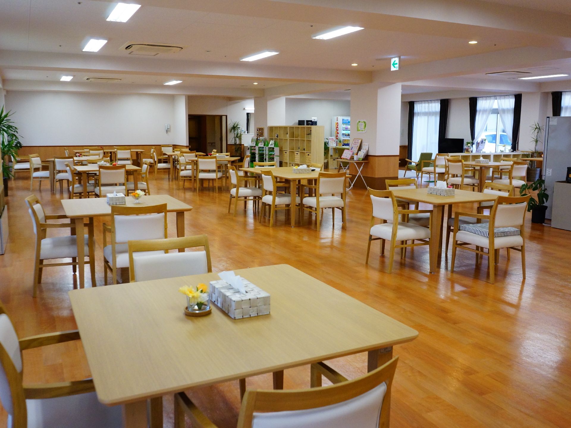 共有で食事やカフェを楽しめるスペースには小さいテーブルに椅子3脚のセットが沢山ある。テーブルに花が置いてあり、華やか。