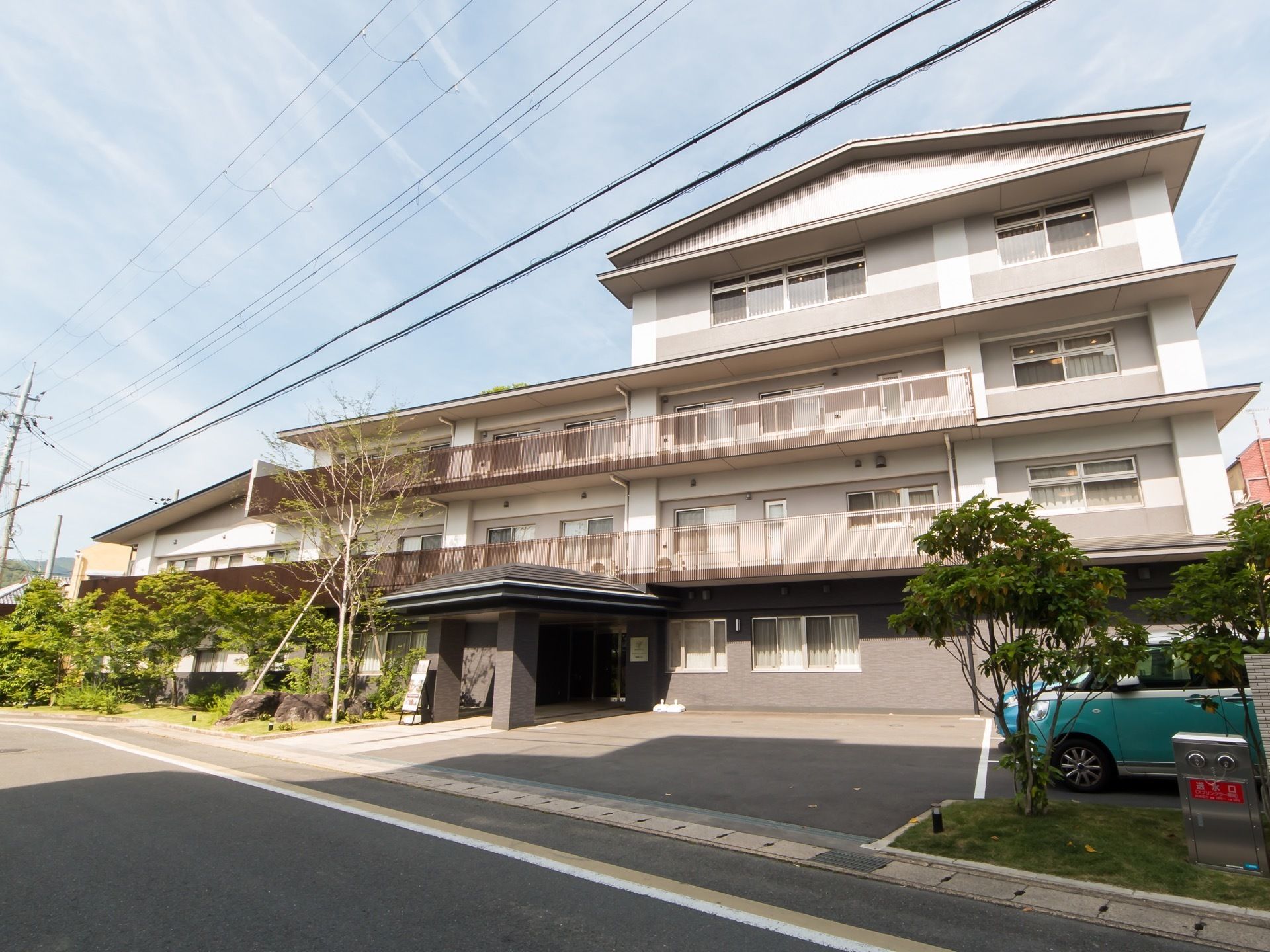 白色と薄い灰色を基調とした外壁で、一部４階建ての施設である。敷地内に車が停まっていて、その近くには消火栓が設置されている。