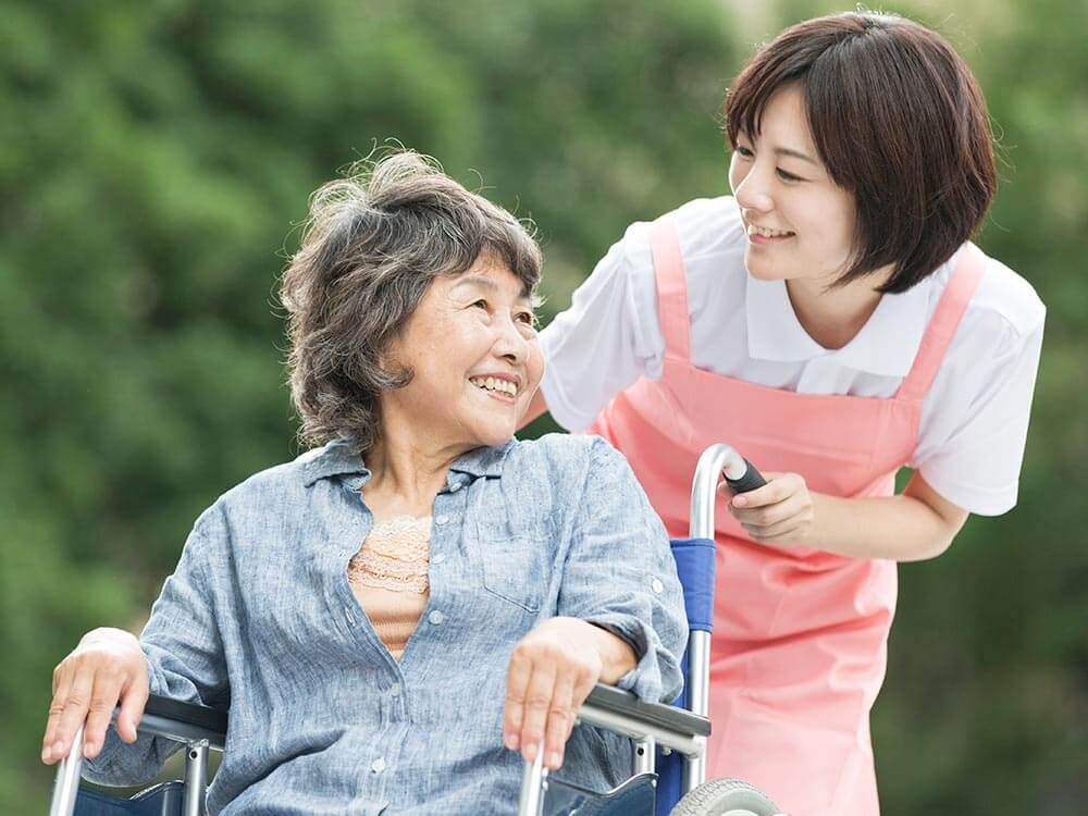 顔を見合わせる車椅子に乗った高齢女性と女性ヘルパー